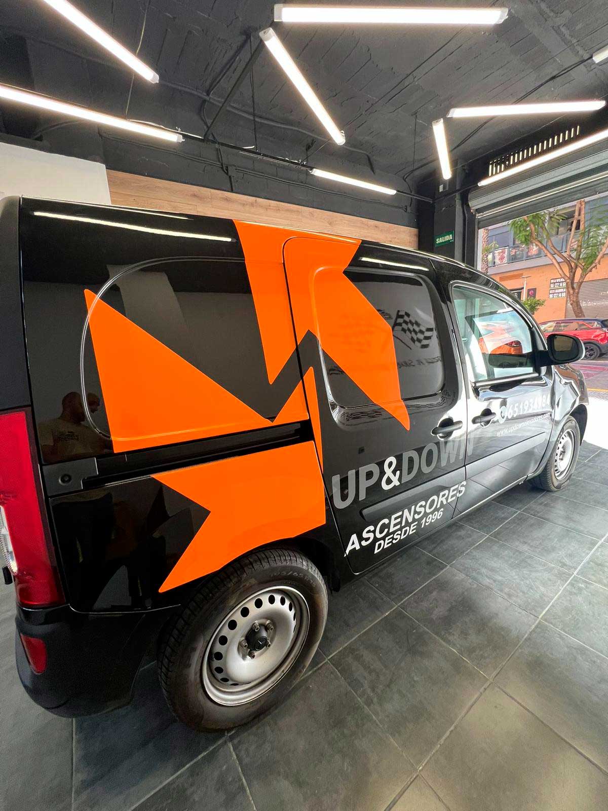 Furgoneta negra rotulada con grandes gráficos naranjas y textos corporativos, instalada por CDW Llacer en su taller.