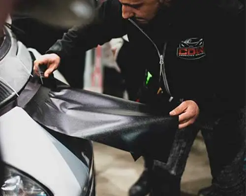 Técnico aplicando una lámina de vinilo negro sobre la carrocería de un coche en proceso de wrapping