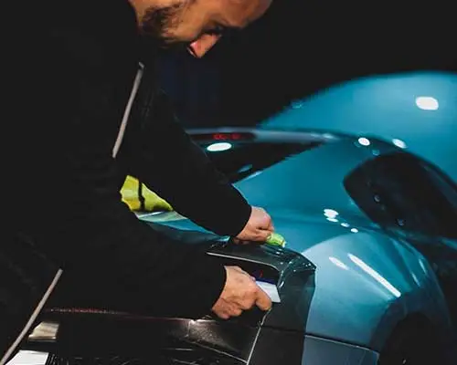 Técnico ajustando film con espátula sobre la carrocería de un coche azul para un acabado limpio